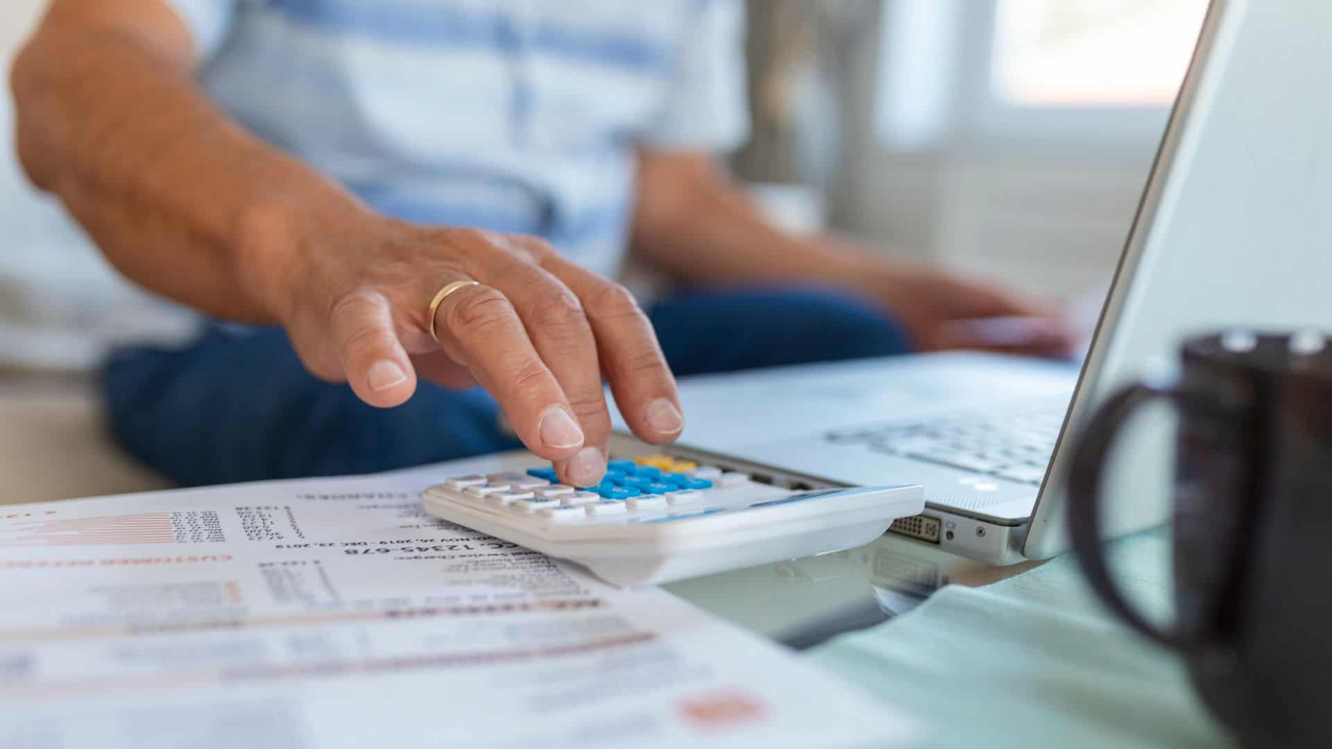 Uomo con calcolatrice e PC calcola le tasse di Airbnb. Foto di stefamerpik
